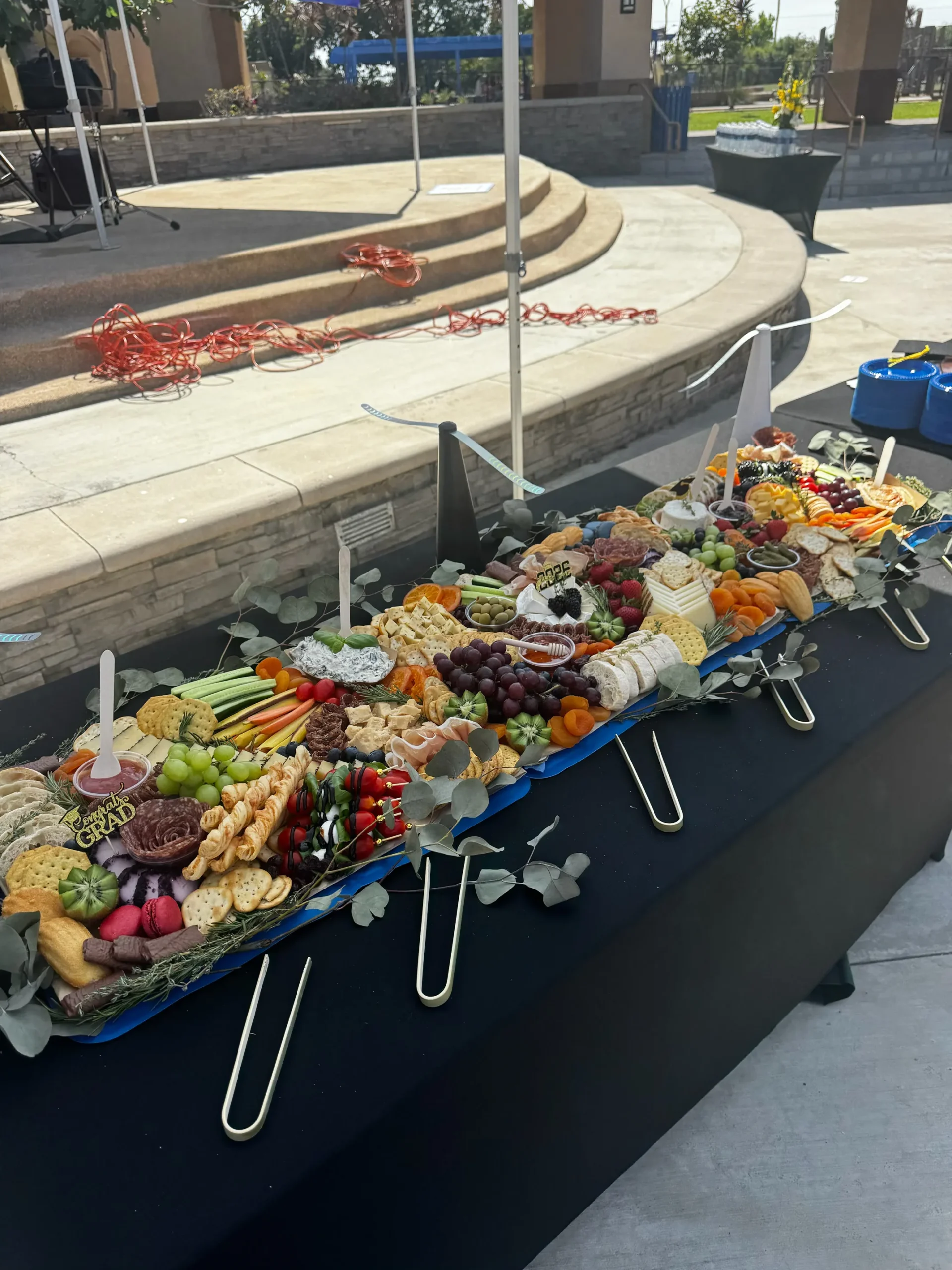 Outdoor graduation grazing table with cheeses, cured meats, fruit and vegetables