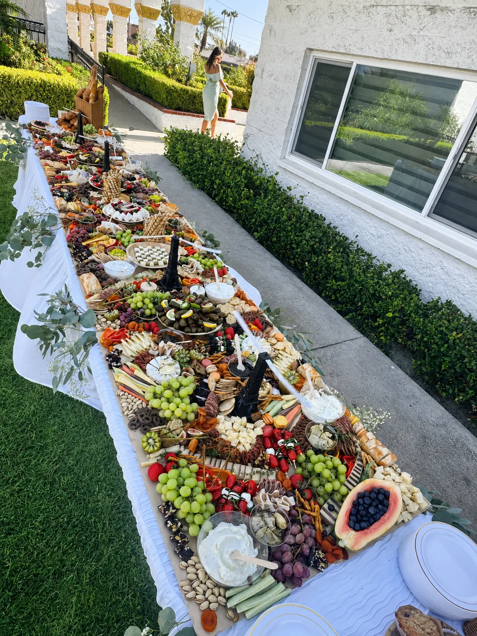 Long outdoor grazing table with charcuterie, cheeses, fresh fruit, vegetables and dips